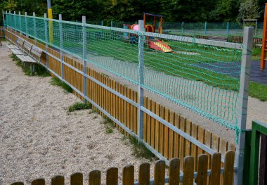 Çocukların oyun parkının çitlerle çevrili olması ve çitin üstünde bir ağ daha olması. Galvanize metal çerçeve yeşil bir tekstil örgüsüyle çitin yüksekliğini arttırır. kum kutusu