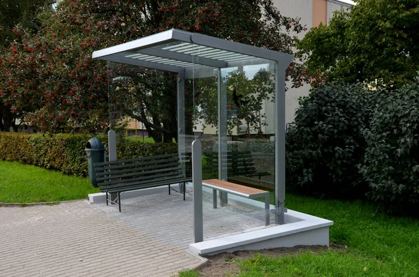 city bus stop. glass shelter with integrated wooden bench. only the roof and the back wall. on the street by the sidewalk in the city. elegant arch, station, platform, lawn, grass, tactile