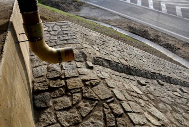 Otoyol köprüsü drenajı. Delikleri olan ses emici bir duvar suyu içeri alır. Oluklar su oluğundan su topluyor. Esnek kauçuk bağlantısı olan boru. Su akışını yavaşlatıyor.