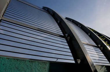 Caddedeki metal kirişlere gömülmüş köprüdeki çizgili camlardan oluşan ses geçirmez bir duvar. Pencereleri basınç vidalarıyla onarıyorum. Gözenekli bloklar yol üzerinde eğimli, çapraz, tırmanma