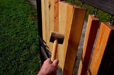 Asılı kütüklerin çeşitli yerel ağaçların kirişleri olduğu bir gölgelik. Diğer tarafta, Çekçe ve Latince bahçıvanlık isimleri. Tahta bir çekiçle dum