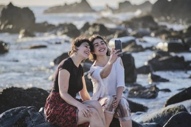 Denizin kıyısındaki bir kayanın üzerinde selfie çeken kardeşler..