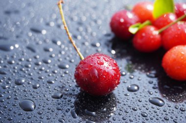 Siyah zemin üzerinde su damlaları olan kiraz meyveleri.