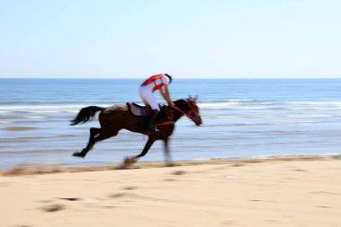 Sahilde dörtnala koşan yarış atı ve jokeyi, sahilde yarışan yarış atları ve jokeyleri