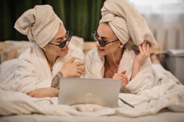 beautiful young woman with her daughter in bathrobe and towel lying on bed in bedroom