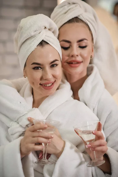 two beautiful women in bathrobes drinking coffee and having fun in spa salon