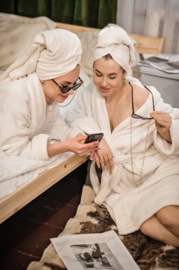 İki kadın, kaplıcada oturup telefonuyla konuşurken akıllı telefondan konuşuyor ve gülümsüyor.