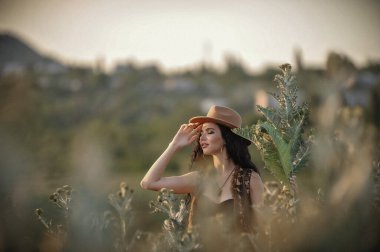 Tarlada poz veren şapkalı ve saman elbiseli güzel bir kadın.