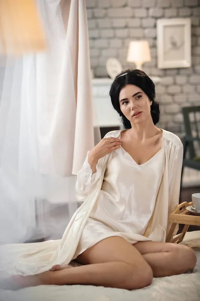 ベッドの上に座っている白いドレスの美しい若い女性 — ストック写真
