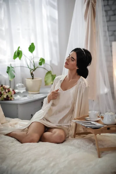 Beyaz Elbiseli Güzel Bir Kadın Yatakta Oturuyor Kameraya Bakıyor — Stok fotoğraf