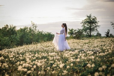 Beyaz elbiseli ve peçeli gelin çayırda yürüyor.