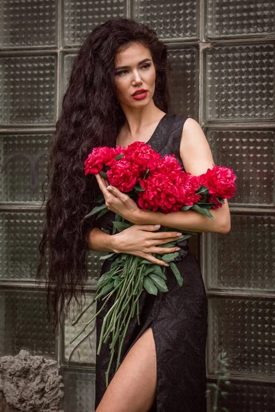 庭に赤いバラを持つ美しい若い女性 — ストック写真