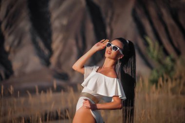 beautiful young woman in a dress and sunglasses posing on the beach
