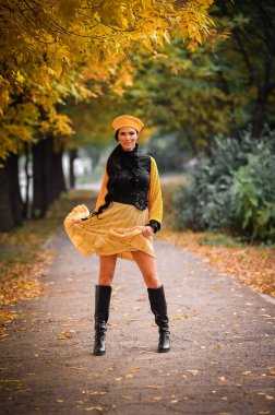 Güz parkında siyah ceketli ve şapkalı güzel bir kız yürüyor.