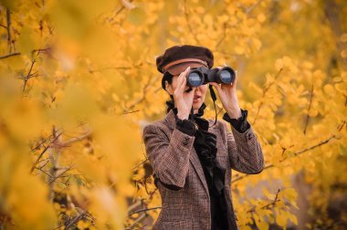 Sonbahar ormanında dürbünlü genç bir kadın.