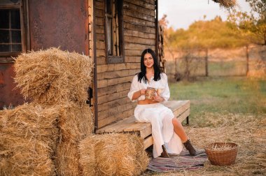 beautiful young woman in a straw hat and a dress with a basket of hay