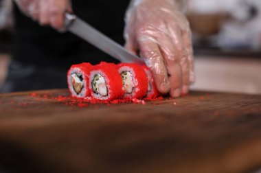 Şef, suşi rulolarını somon ve sosla keser.