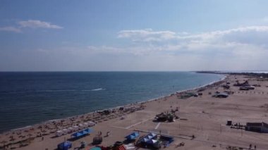 İnsanlar güneşlenir, bulutlu bir günde öğleden sonra sahilde yüzerler. Eylül ayında kumlu bir plajda turistlerin hava görüntüsü.