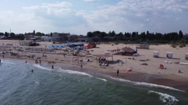 İnsanlar sahilde yüzer. Plaj insanları güneşleniyor, güneşleniyor, Eylül 'de öğleden sonra deniz kenarında dinleniyorlar. Deniz dalgaları ve kum. Orijinal video 4k, 29.97 fps.
