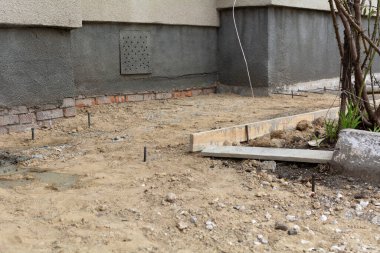 Bir evin temelleri için kör bir alan inşa etme süreci. Kum, ezilmiş taş, demir tesisatı ve kör bir alan oluşturmak için ahşap döşeme tahtaları..