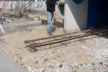 Tiraspol, Moldova - 30 Mart 2022: Kimliği belirsiz inşaatçı bir binanın girişine yakın bir kürekle kum ve çakıl döşedi. Evin temelinin kör noktasını inşa etme süreci..