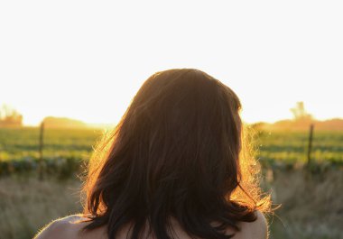 Arkadan gün batımını seyreden bir kadın. Yazın yeşil tarlada.