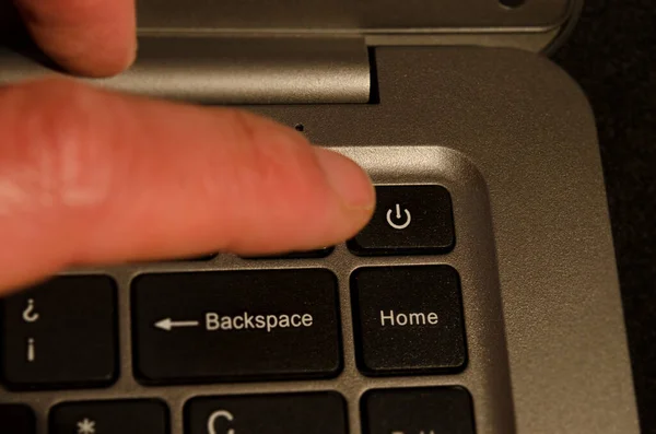 laptop power key, hand about to press it to turn off the notebook doing work from home