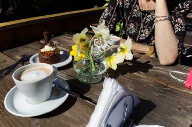 Kahveli açık kafe masası, Markiz keki ve çiçek aranjmanı.