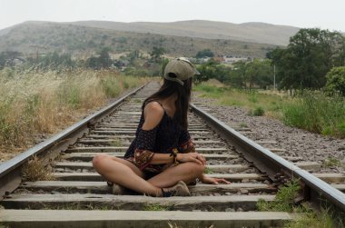 Tren raylarında oturan kadın, yolun uçsuz bucaksızlığına bakıyor.