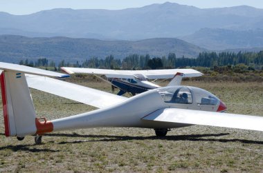 Bariloche Havalimanı 'nın arka planında dağlar olan pervaneli bir uçak tarafından çekilmek üzere olan ultralight planörü.