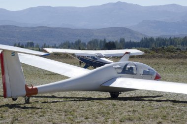 Bariloche Havalimanı 'nın arka planında dağlar olan pervaneli bir uçak tarafından çekilmek üzere olan ultralight planörü.