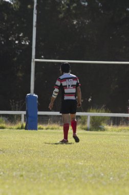 Rugby oyuncusu sahada yürüyor, arka planda rugby golü var.