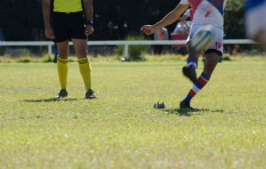 Rugby oyuncusu yanında hakemle topa vuruyor.