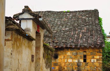 Gri kiremit çatılı eski bir ev. Sarı-kahverengi çizgili beyaz duvarlar. Jujing Köyü, dağlarla ve suyla çevrili tipik küçük yuvarlak bir köydür. Wuyuan, Jiangxi, Çin.