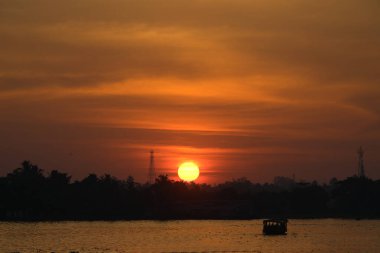 Gün batımında turuncu güneş. Gölde yüzen bir yüzen evin silueti. Kerala 'daki kayıkhane (Kettuvallam olarak bilinir), Hindistan' ın güneybatısında. Ocak 2018