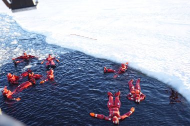 Kırmızı kuru bir hayatta kalma elbisesiyle buz gibi kutup denizinde yüzüyor. Bir buz kırıcı (buz kırıcı gemi) ile Kuzey Kutbu sularını keşfetmek.