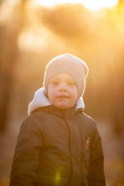 Sonbahar sokağında ceketli bir çocuk gülümsüyor.