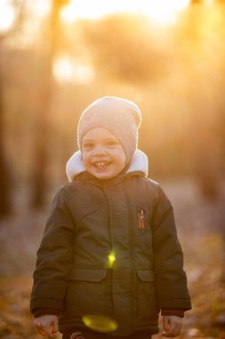 Sonbahar sokağında ceketli bir çocuk gülümsüyor.