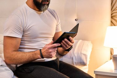 Yatakta e-kitap okuyan sakallı bir adam kahve ya da kahve masasında bir fincan kahve ile...