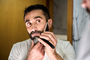 Sakallı genç bir adam aynanın önünde geleneksel bir bıçakla tıraş oluyor. Yüksek kalite fotoğraf