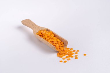 Beyaz arka planda ahşap bir kaşıkta kırmızı parçalanmış mercimek, insan yok.