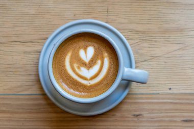 Kapuçino bardağı ve ahşap masa üzerinde latte resmi, yukarıdan çekilmiş, yatay.