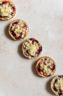 Five home baked plum crumble tarts in diagonal shape from above