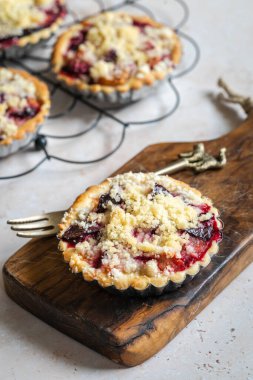 Several home baked plum crumble tarts on cooling rack with fork