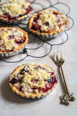 Several home baked plum crumble tarts on cooling rack with fork