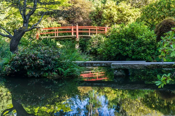 A red walking bridge and pond in a garden in Seattle, Washington.