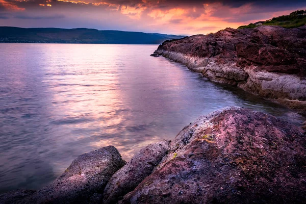 Wemyss Körfezi 'nde yansıtıcı sakin deniz manzaralı parlak turuncu gün batımı İskoçya, İngiltere' de kayalık kıyı şeridi.