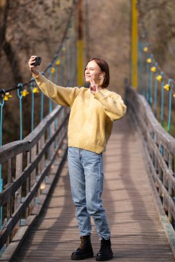 Bir kız blogger sonbahar ormanında cep telefonundan canlı yayın yapıyor. Genç bayan parktaki telefona bakıyor..