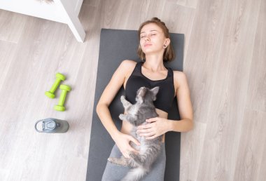 Güzel, ince bir kız evcil bir kediyle yoga yapıyor ve meditasyon yapıyor. Evcil bir hayvanla evde eğitim..
