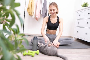 Güzel, ince bir kız evcil bir kediyle yoga yapıyor ve meditasyon yapıyor. Evcil bir hayvanla evde eğitim..